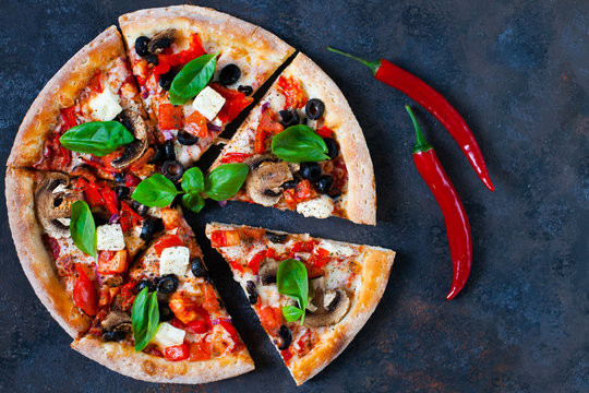 Hot testy pizza with tomatoes, mozzarella, mushrooms, olives, red pepper and basil on black concrete background. Copyspace. Top view.