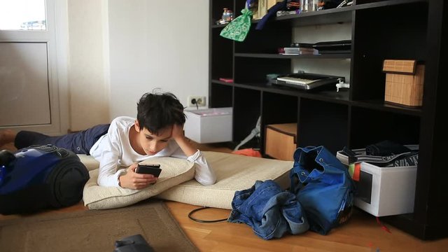 Boy teenager is shirking her homework, playing on her mobile phone. Cleaning of the children's room. Disorder in the teen room