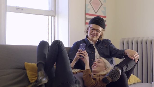 Trendy Young Woman Relaxes On Couch With Her Boyfriend, She Takes Photos Of Her Legs In the Air