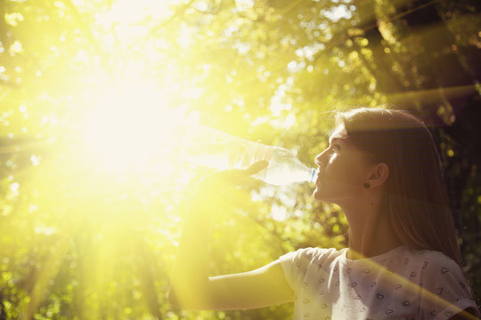 Young beautiful sports girl drinks drinking water in sunlight during morning jogging