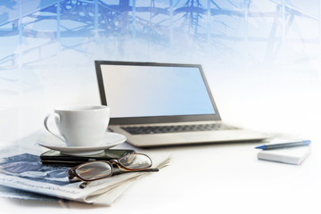 business office workspace, laptop, cell phone, newspaper, glasses and coffee cup on a white desktop, in front of a blue industry background, copy space