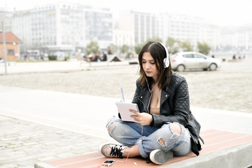 Fototapeta premium Young woman listening music from a smart phone and writing notes