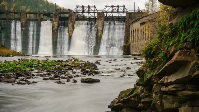 PAN time lapse of water pours like ribbons over the old power generation dam with lush green moss covered rocks in the background.