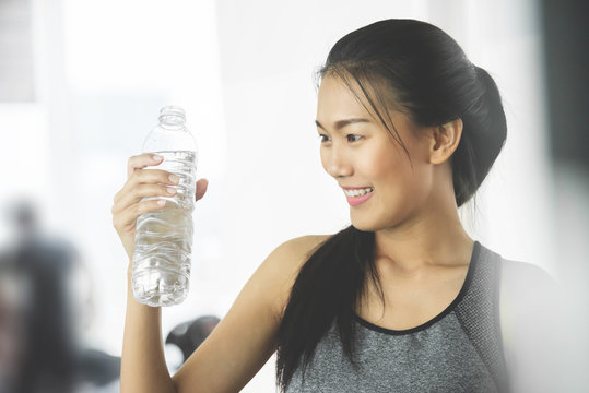 Asian woman in sportswear holding bottle of water at the gym.