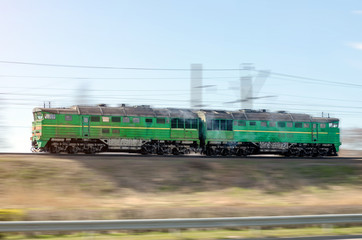 Fototapeta na wymiar Train double locomotive, green rides at speed by rail.