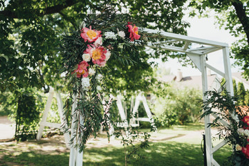 A composition of flowers and greenery adorns the arch for the wedding ceremony, which stands under a tree