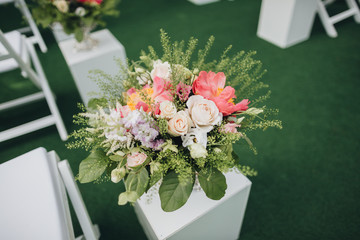 A composition of flowers and greens in a vase stands among the chairs for guests in the area of the wedding ceremony