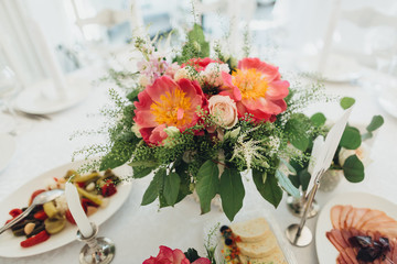 On the festive table in the wedding banquet area there are compositions of flowers, candles, plates, cutlery, napkins