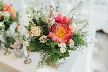 On the festive table in the wedding banquet area there are compositions of flowers and greenery, next are the candles