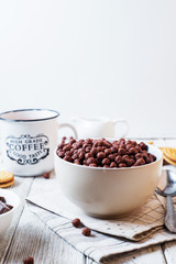 Hearty and tasty breakfast for children, cornflakes, chocolate balls with milk, cocoa and biscuits on a light wooden background 