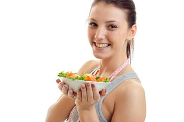 Portrait of a remarkable young girl who laughs and holds a large plate of vegetable salad closeup