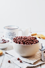 Hearty and tasty breakfast for children, cornflakes, chocolate balls with milk, cocoa and biscuits on a light wooden background 