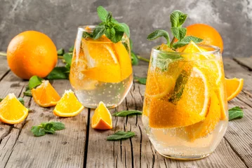 Fototapeten Summer refreshing orange drink. Detox, diet, infused. Variations on lemonade. Mineral water with pieces of fresh orange and mint. On a rustic wooden table with grey wall. Vertical, copy space © ricka_kinamoto