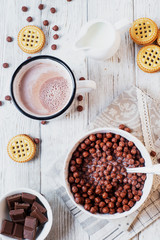 Hearty and tasty breakfast for children, cornflakes, chocolate balls with milk, cocoa and biscuits on a light wooden background 