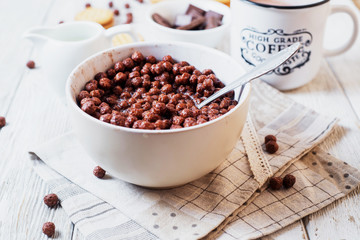 Hearty and tasty breakfast for children, cornflakes, chocolate balls with milk, cocoa and biscuits on a light wooden background 