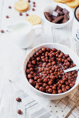 Hearty and tasty breakfast for children, cornflakes, chocolate balls with milk, cocoa and biscuits on a light wooden background 