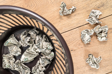 Crumpled dollars on a wooden table and in a plastic trash can close up