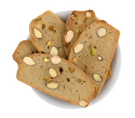 Almond pistachio crisp bread slices in a small bowl isolated on a white background.
