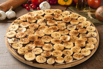 Sweet raw pizza with banana and cinnamon on wooden background