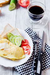 Hearty and tasty breakfast, traditional in the hotel, omelette from chicken eggs with cheese, fresh vegetables - cucumber and tomato, white toast and black coffee on a light wooden background