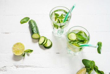 Cold and refreshing infused detox water with lime, mint and cucumber in a glass on wood background