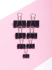 black paper clips on light pink and white background. top view. flat lay. 