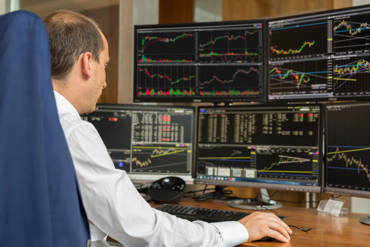 Rear view of stock trader looking and analyzing stock data at multiple computer screens.