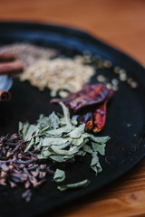Green curry leaves on black metal plate surrounded by other spices.