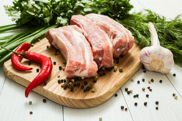 Raw pork ribs with vegetables and greens on a wooden board. Cooking barbecue.