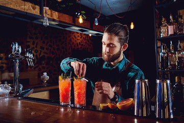 Bartender with a beard makes a cocktail behind counter in the bar.