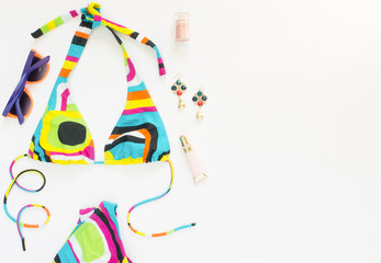 Summer outfit, beach outfit, summer stuff. Geometric abstract pattern swimsuit, bright sunglasses and earrings. Flat lay, top view.