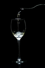 Wine is pouring from a bottle into a glass on a black background, studio light