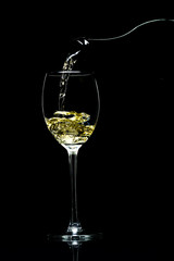 Wine is pouring from a bottle into a glass on a black background, studio light