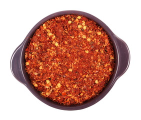pile crushed red cayenne pepper, dried chili flakes and seeds in porcelain dish isolated on white background