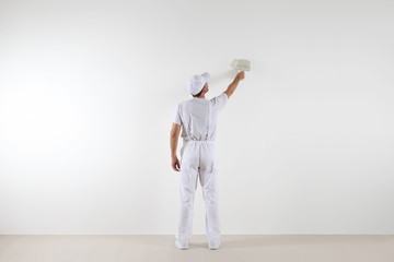 Rear view of painter man looking and painting blank wall, with paint brush, isolated on white big...