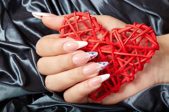 Hand with long artificial french manicured nails holding a heart 