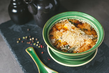 Appetizing fish soup with sesame seeds in green porcelain plate on the gray background. Japanese cuisine.