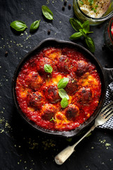 Meatballs in tomato sauce with addition cheese and fresh basil on iron pan, black background