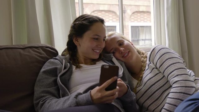 Happy Friends Cuddle On Couch And Take Selfie Together, Scroll Through Photos 