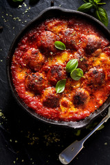 Meatballs in tomato sauce with addition cheese and fresh basil on iron pan, black background