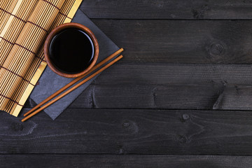 Background for sushi. Bamboo mat, soy sauce, chopsticks on dark table. Top view with copy space © xamtiw