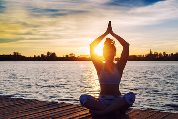 Fototapeta na wymiar Young woman doing yoga exercises on the lake beach at sunset