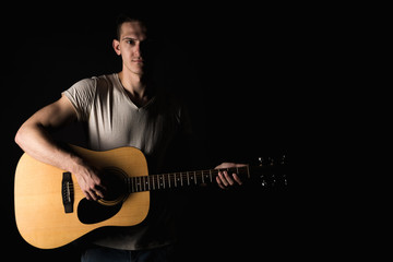 Guitarist, music. A young man plays an acoustic guitar on a black isolated background. Horizontal frame