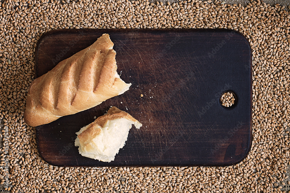 Wall mural broken bread on a kitchen board against a background of wheat grains