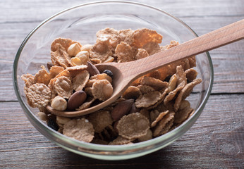 Oat flakes in bowl and wooden spoon with mix nuts and dry fruits on wooden background.