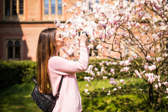 Happy woman traveler take photos by camera with cherry blossoms tree on vacation while spring