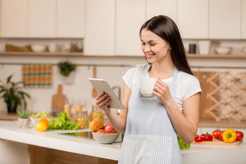 Obraz na płótnie Canvas Young Woman in kitchen with tablet computer looking recipes, smiling. Food blogger concept