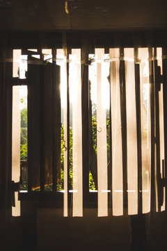 Morning sun shining through a window and wooden shutters onto mosquito nets and curtains in a jungle lodge in Sri Lanka.