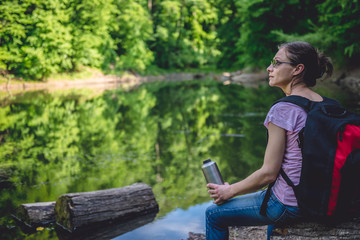 Fototapeta premium Woman sitting on a tree log by the lake