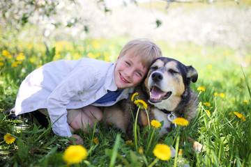 Happy Little Boy Relaxing in Flower Meadow and Hugging his Pet Dog